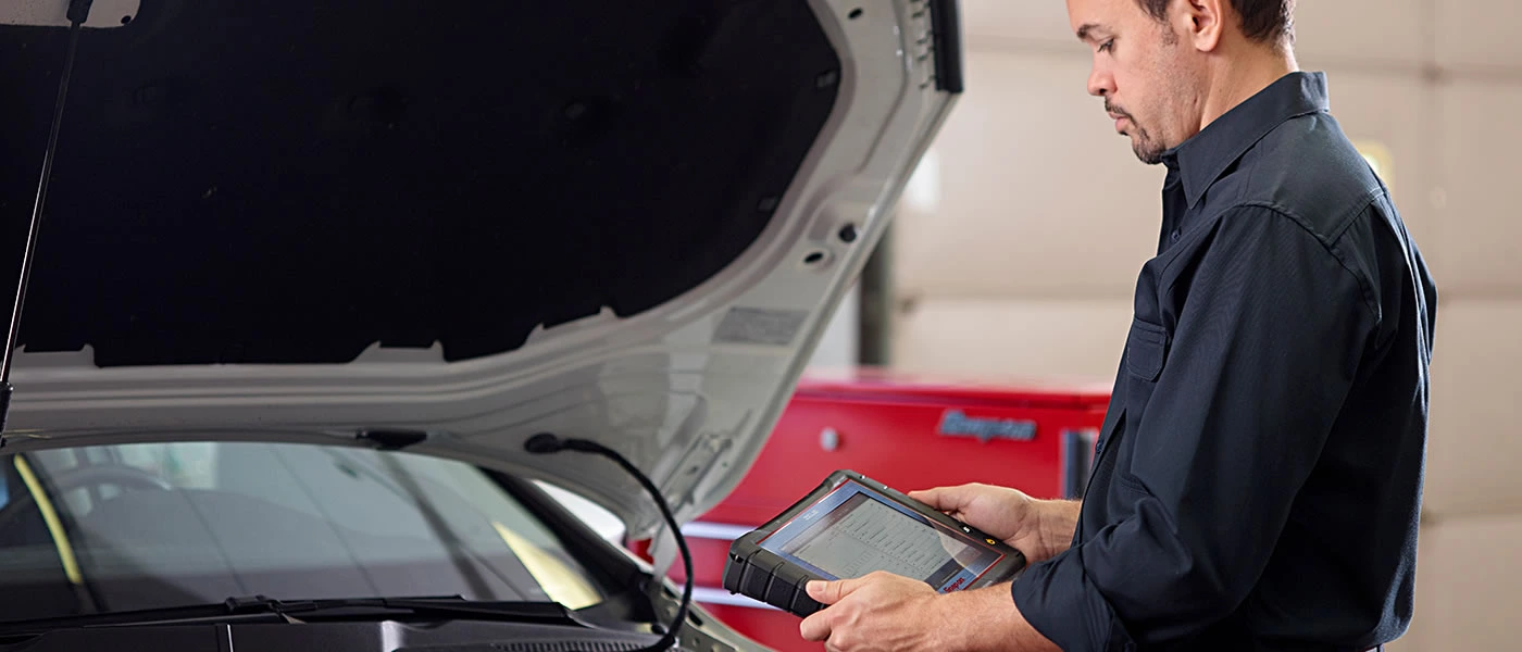 Automotive associate completing Intelligent Diagnostics using a Snap-on scanner under the hood of a vehicle
